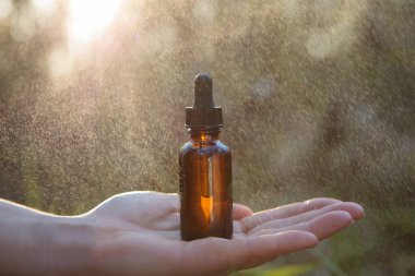 Background blurring of a hand holding an essential oil and a bottle.