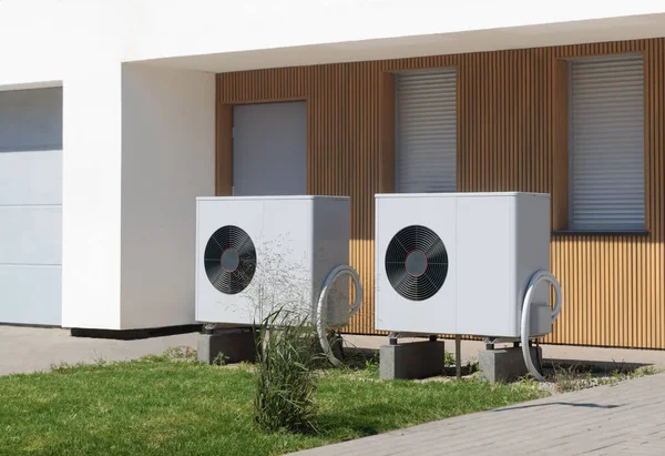 Two eco-friendly air source heat pumps situated in front of a modern house with a lush lawn, symbolizing green heating solutions.