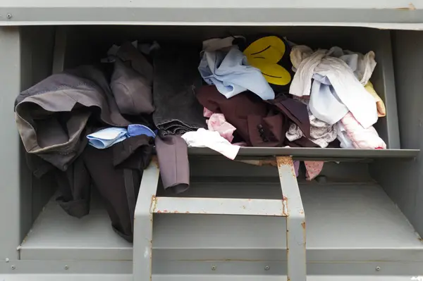 stock image Mixture of different clothing items inside a metal donation bin for recycling.