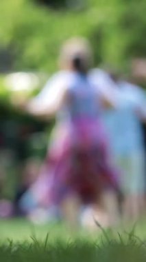Çimlerin üzerinde dans eden, hareket ve neşeyi yakalayan insanların bulanık siluetleri..
