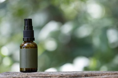 Üzerinde boş etiket olan kahverengi bir cam sprey şişenin yakın plan resmi. Tahta bir yüzeye yerleştirilmiş, yeşil, bulanık bir arka plan..