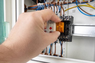Görünür kablolar ve bileşenleri olan bir kontrol paneline elektrik rölesi yerleştiren bir eli kapat.