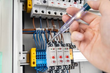 Electrician Testing Electrical Connections with Voltage Tester in Control Panel clipart