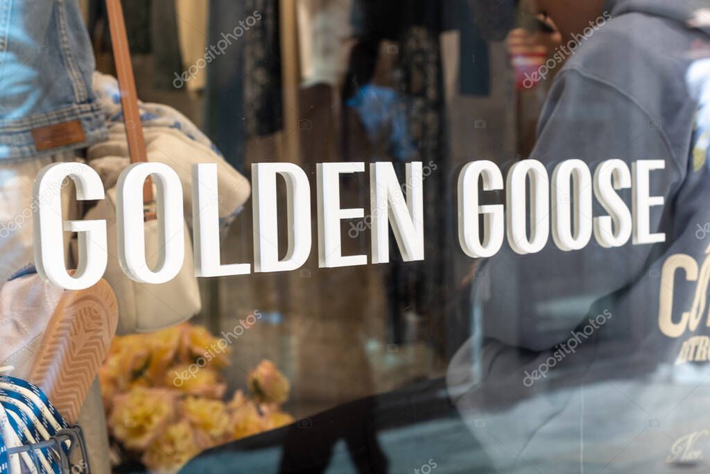 Venice, Italy - April 20 2025: Golden Goose store logo on glass window with interior view and shoppers