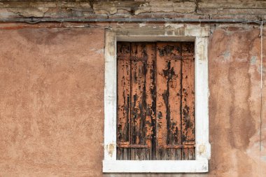 Ağır yıpranmış ahşap panjurları ve kırsal duvar dokusuyla eski bir pencere.