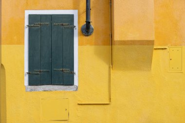 Burano İtalya 'da yeşil panjurlu sarı desenli bir duvar.