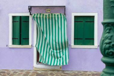 Burano İtalya 'da yeşil kepenkleri ve çizgili perdesi olan mor ev cephesi