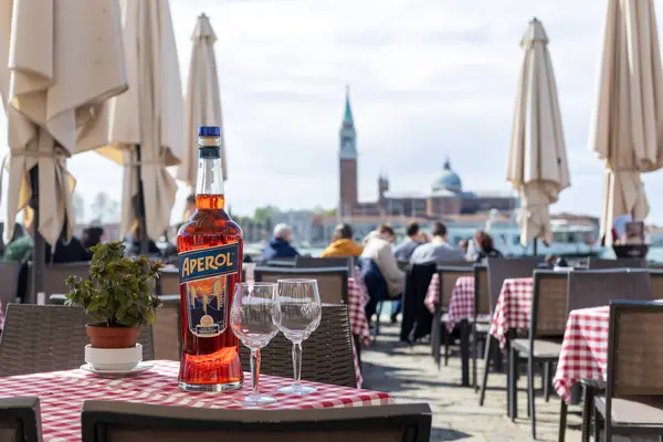 Venedik, İtalya - 18 Nisan 2025: Arka planda turistler bulunan açık kafeterya masasında Aperol şişesi