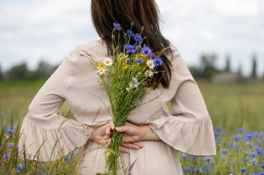 Arkasında kır çiçekleri tutan bir kadın.