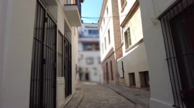 İspanya, Katalonya 'da, Costa Dorada, Sitges' de dar bir sokakta yürüyorum. Beyaz duvarları ve Akdeniz geleneksel evleri olan pitoresk cadde