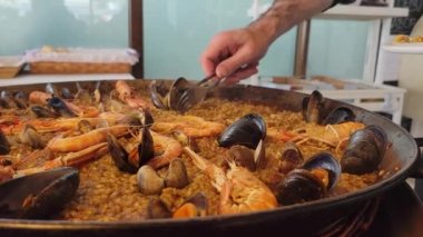 Paellera 'dan tipik bir İspanyol deniz mahsulü paella servisi yapan bir garsonun resmi. Paella tavası, öğle yemeği için sete konmuş.