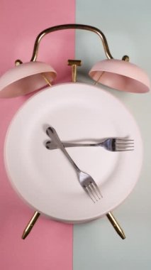 Alarm clock and a rotating plate with fork and knife. Time to eat, diet or Intermittent Fasting concept. Vertical video.