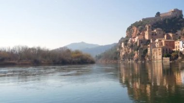 Old town of miravet with the templar castle on the top and the ebro river flowing quietly on a sunny day.