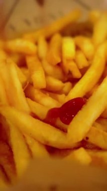 Parşömen kağıdında servis edilen patates kızartmasının üzerine ketçap sosu dökmek. Popüler fast food, bol kızarmış patates cipsi. Dikey video