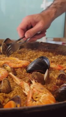 Paellera 'dan tipik bir İspanyol deniz mahsulü paella servisi yapan bir garsonun resmi. Paella tavası, öğle yemeği için sete konmuş. Dikey video