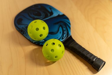 Pickleball ekipmanları. Pickleball, tenis kortunun dörtte biri büyüklüğünde bir kortta oynanan kürek ve Whiffleball ile oynanan popüler bir Amerikan sporudur..