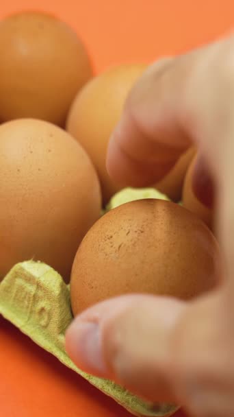 手从橙色背景的打开的蛋盒中取出一个鸡蛋 收缩膨胀的概念 物品大小或数量减少的过程 垂直录像 — 图库视频影像