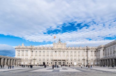 Madrid, İspanya. 08 Aralık 2023: İspanya 'nın tarihi bir simgesi olan Madrid Kraliyet Sarayı' nı ziyaret eden turist kalabalığı. Görüntü, sarayın beyaz ve süslü cephelerini gösteriyor. Sütunlar, heykeller...