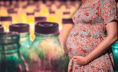 Arka planda bulanık plastik bir şişeyle hamile karnının yakın çekimi. Düşük düzeyde mikro plastik ve BPA bebeklerin ve bebeklerin normal gelişimi için zararlı olabilir.