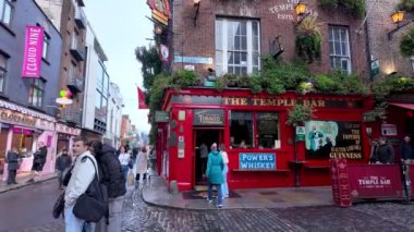 Dublin, İrlanda. 17 Nisan 2024: İrlanda 'nın ünlü barının önünde yürüyen turistler İrlanda başkentinin merkezindeki Tapınak Bar - erkek turistler kadın turistler. Dikey video.