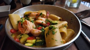 Bir tabak Paccheri al Profumo di Mare 'ye rendelenmiş parmesan peyniri koymak. Tabakta al dente makarna, sulu karides ve aromatik otlarla süslenmiş taze sebze karışımı var.