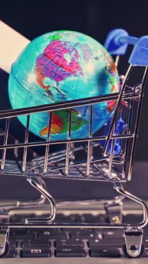 Dünya küresi, online alışveriş ve seyahat rezervasyonlarının kolaylığını sembolize eden, açık bir dizüstü bilgisayar klavyesine yerleştirilmiş, küresel pazar yerimizi gösteren minyatür bir alışveriş arabasının içine yerleştirilmiş.