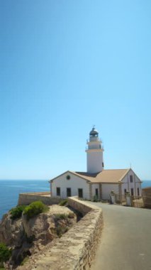 Capdepera Deniz Feneri, Mallorca 'daki engin ve sakin Akdeniz manzaralı engebeli bir uçuruma tünemişti. Berrak mavi gökyüzü ve sakin sular dingin ve büyüleyici bir manzara yaratır.