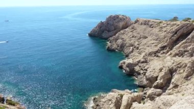 Punta des Castellas 'ın engebeli uçurumları ve turkuaz suları Mallorca adasının doğu kıyılarında. Açık mavi gökyüzü ve sakin Akdeniz sakin ve resimli bir kıyı manzarası yaratır.