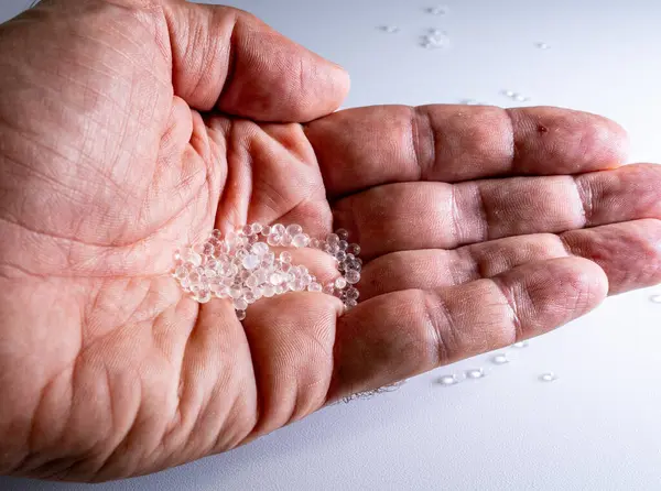 Beyaz bir zemine karşı temiz plastik topaklar sunan bir elin yakın plan görüntüsü, su cisimlerindeki yaygın mikroplastik kirliliği ve bunun küresel çevre üzerindeki etkisini sembolize ediyor