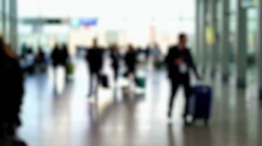 Dolu bir havaalanı terminalinin bulanık görüntüsü. Gezginler yürüyor ve çantaları taşıyor. Dinamik ve hareketli bir atmosfer yaratıyor..