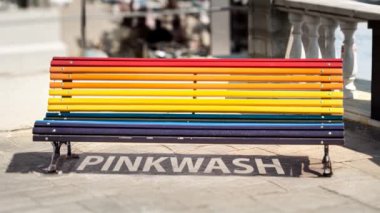 Gökkuşağı kürsüsü LGTBQ haklarını sembolize ediyor ama aynı zamanda Pinkwash yazısıyla gölge düşürüyor. Şirketlerin LGBTQ haklarını desteklediklerini iddia ettikleri bir uygulama olan pembe yıkamayı kınama kavramı