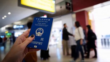 Kadının elinde Hong Kong pasaportu var. Havaalanındaki yoğun bir terminalde yürüyor.