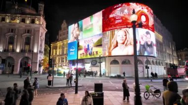 Londra, İngiltere. 20 Ekim 2024: Piccadilly sirk panoları geceleri yayalar ve kırmızı çift katlı otobüslerle reklam değiştiriyor.