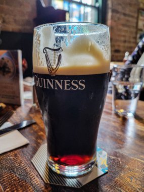 Dublin, Irealnd. April 14, 2024: Close-up of a freshly poured pint of Guinness in a rustic pub setting, featuring warm lighting and a relaxed atmosphere. clipart