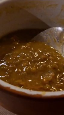 Şef kahverengi seramik kaseden kaşıkla mercimek kaldırıyor. Dikey video