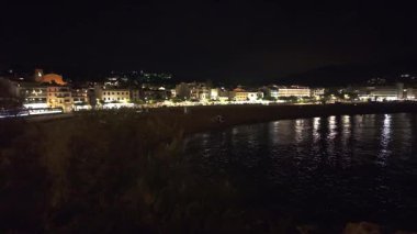 Costa Brava 'da popüler bir turizm merkezi olan Tossa de Mar' ın gece manzarası aydınlatılmış plajını ve tarihi şehir duvarlarını vurguluyor.