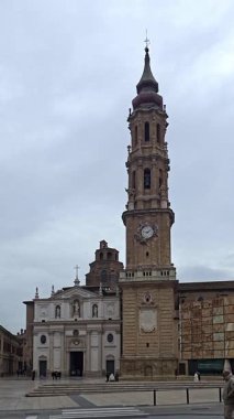 Zaragoza, İspanya. 28 Şubat 2025: Arka planda Zaragoza katedrali saat kulesiyle Plaza de la seo 'da yürüyen turistler