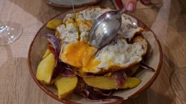 İspanyol tapas yemeği, huevos rotos, patatesler ve İber jambonu üzerine kızarmış yumurta kırarak...