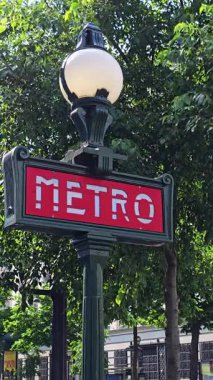 Paris, Fransa. 14 Mayıs 2025, Paris 'teki yemyeşil ağaçlara karşı kırmızı arkaplan ve beyaz harflerle süslü yeşil metro tabelası.