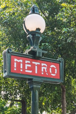 Paris, Fransa. 14 Mayıs 2025, Paris 'teki yemyeşil ağaçlara karşı kırmızı arkaplan ve beyaz harflerle süslü yeşil metro tabelası.