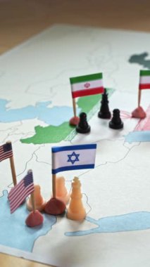 Chess pieces and small flags of Iran, Israel and United States on a map, representing international relations and potential conflict