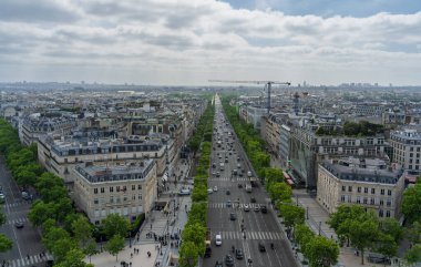 Paris, Fransa. 15 Mayıs 2025: Paris des Champs Elysees Bulvarı 'nda asfalt yolda giden arabalarla bulutlu gökyüzünün altında arka planda inşaat vinci var.