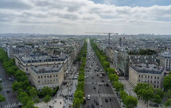 Paris, Fransa. 15 Mayıs 2025: Paris des Champs Elysees Bulvarı 'nda asfalt yolda giden arabalarla bulutlu gökyüzünün altında arka planda inşaat vinci var.