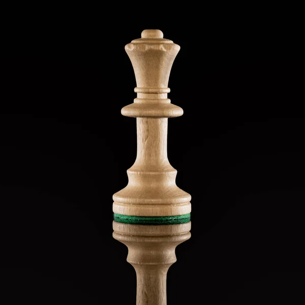 Wooden white chess queen isolated at dark background with transparent reflection on the floor