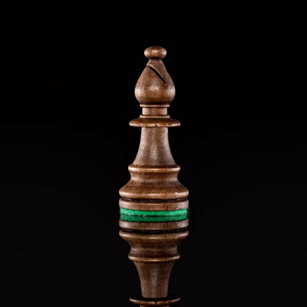 Wooden black chess bishop isolated at dark background with transparent reflection on the floor