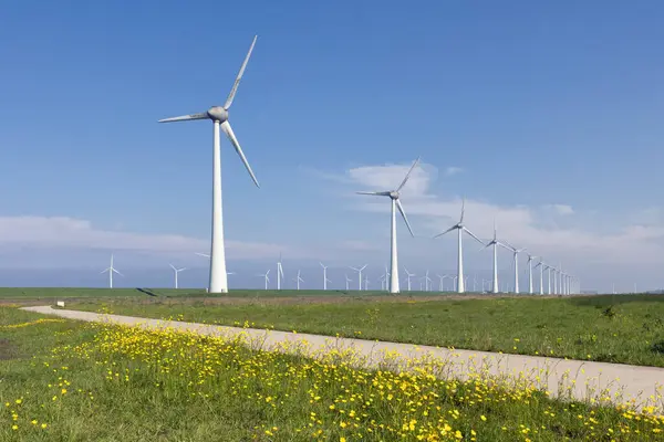 stock image Dutch countryfield in spring with yellow dandelions and big wind turbines