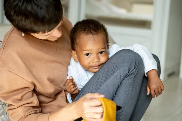 Caring caucasian woman hugging pretty African American baby boy, mother playing with her little son on the floor, family, adoption program