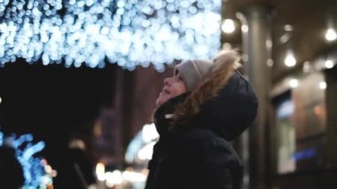 Çocuk gece sokakta duruyor ve Noel ışıklarının, şenlikli atmosferin tadını çıkarıyor. Noel ve Yeni Yıl kavramı