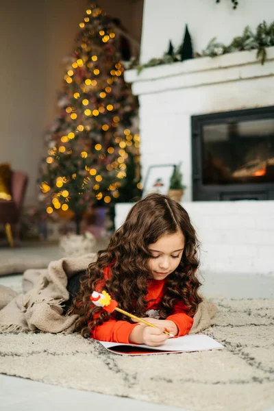 Little girl in Santa hat writes letter to Santa Claus