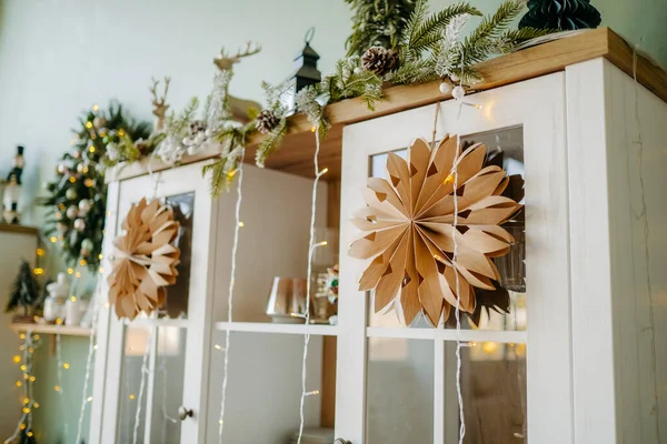Handmade paper swedish stars and garlands, Scandinavian decoration. Atmospheric Christmas time. Stylish paper stars and lights hang from the window in a festively decorated boho room.
